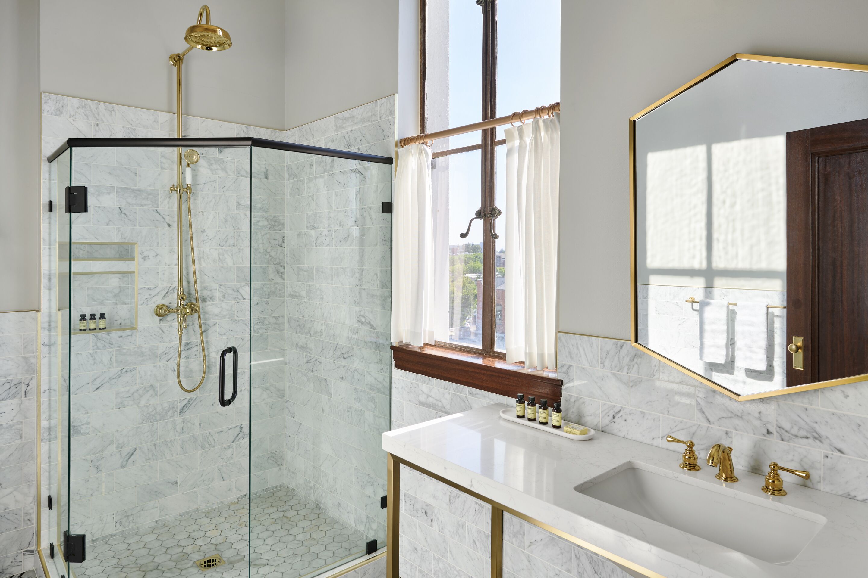 Une salle de bain moderne avec une douche à parois de verre, un lavabo en marbre blanc agrémenté de robinetterie dorée et un grand miroir avec un cadre doré.