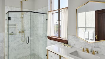 Une salle de bain moderne avec une douche à parois de verre, un lavabo en marbre blanc agrémenté de robinetterie dorée et un grand miroir avec un cadre doré.