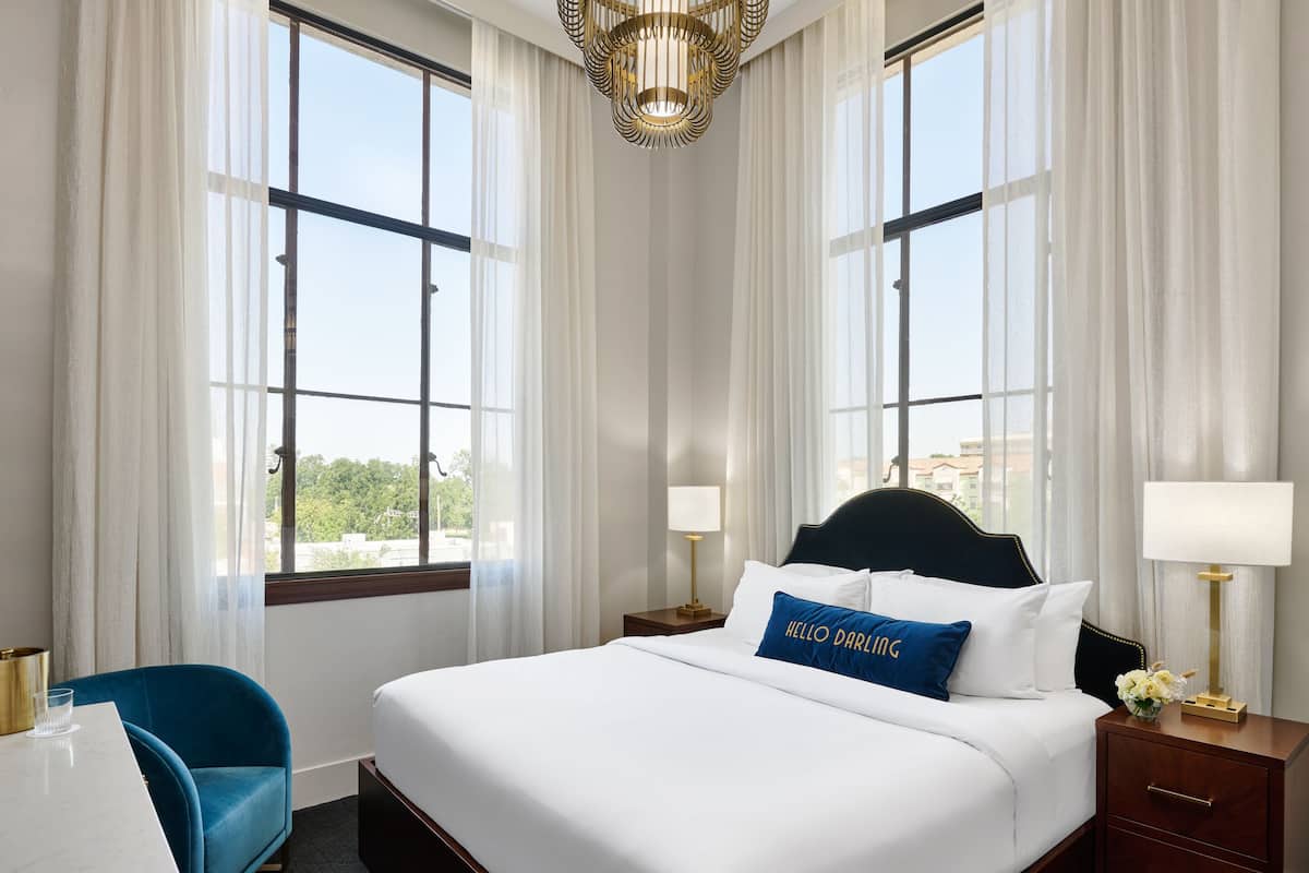 A hotel room with a large bed, two bedside tables, a chair, and a view of the city.