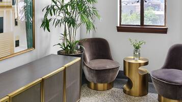 Una habitación moderna con una planta grande en maceta, dos sillones tapizados, una mesita auxiliar y un ventanal con vistas a la ciudad.