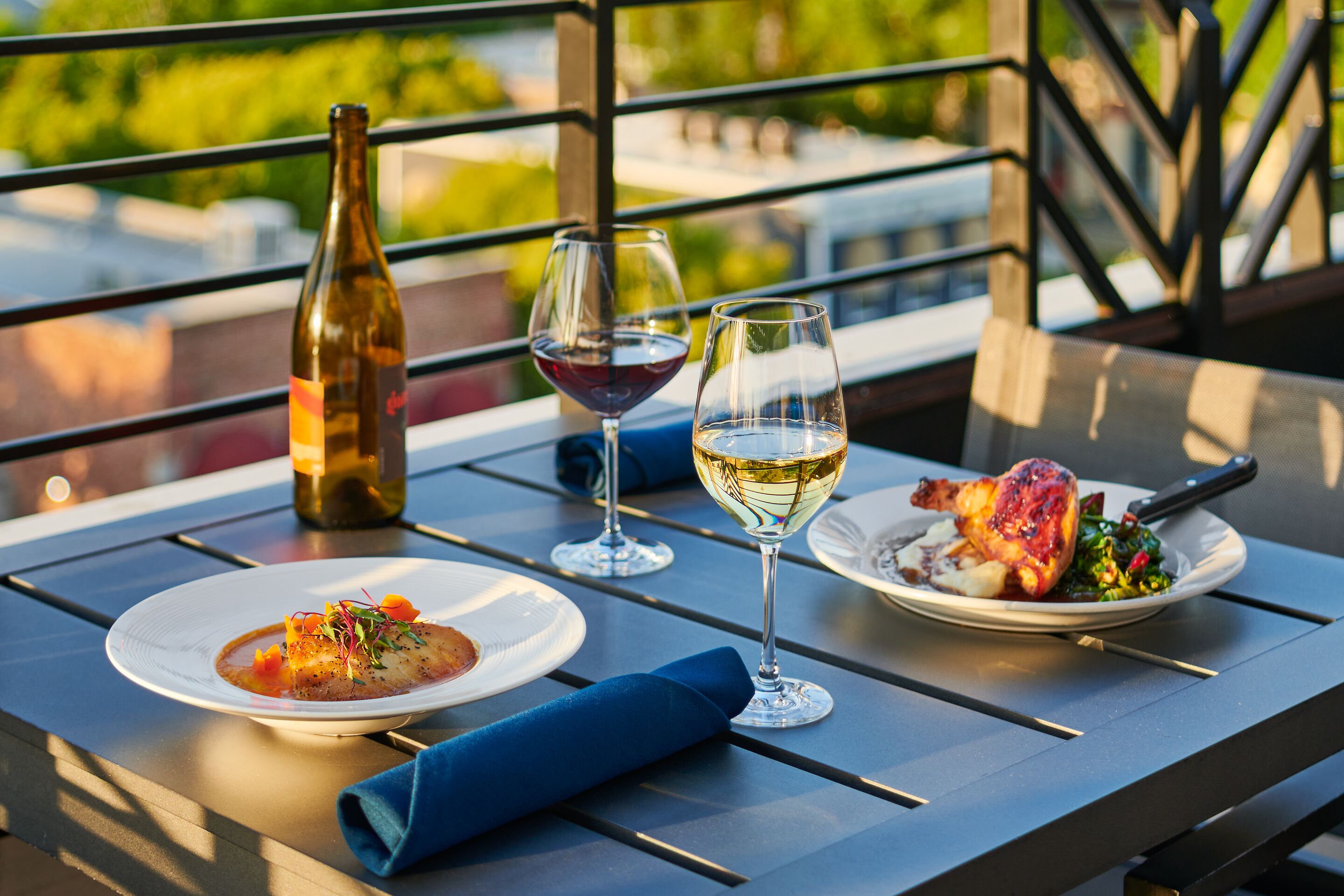 A table with two plates of food, two wine glasses, and a bottle of wine.