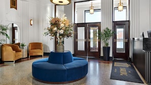 Un hall d’entrée avec un canapé bleu, deux fauteuils, un grand vase rempli de fleurs et un comptoir d’accueil.