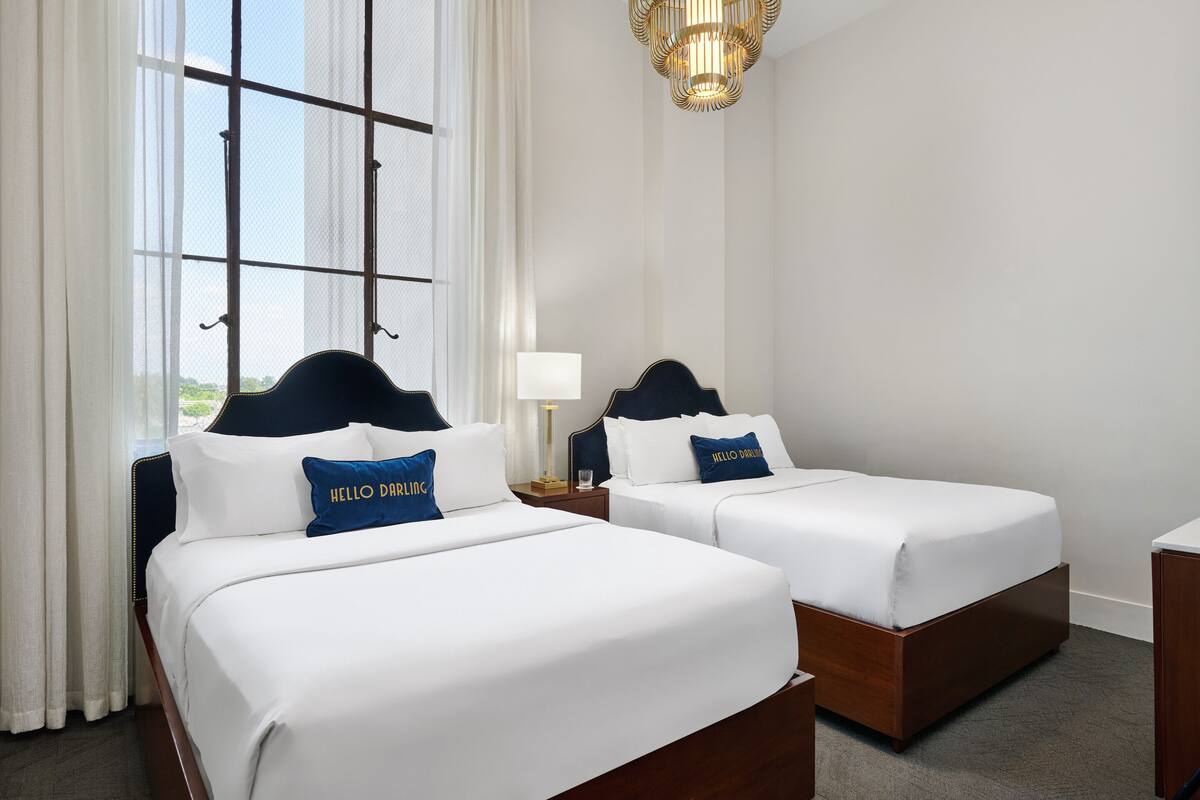 A hotel room with two beds, white bedding, and a view through a large window.