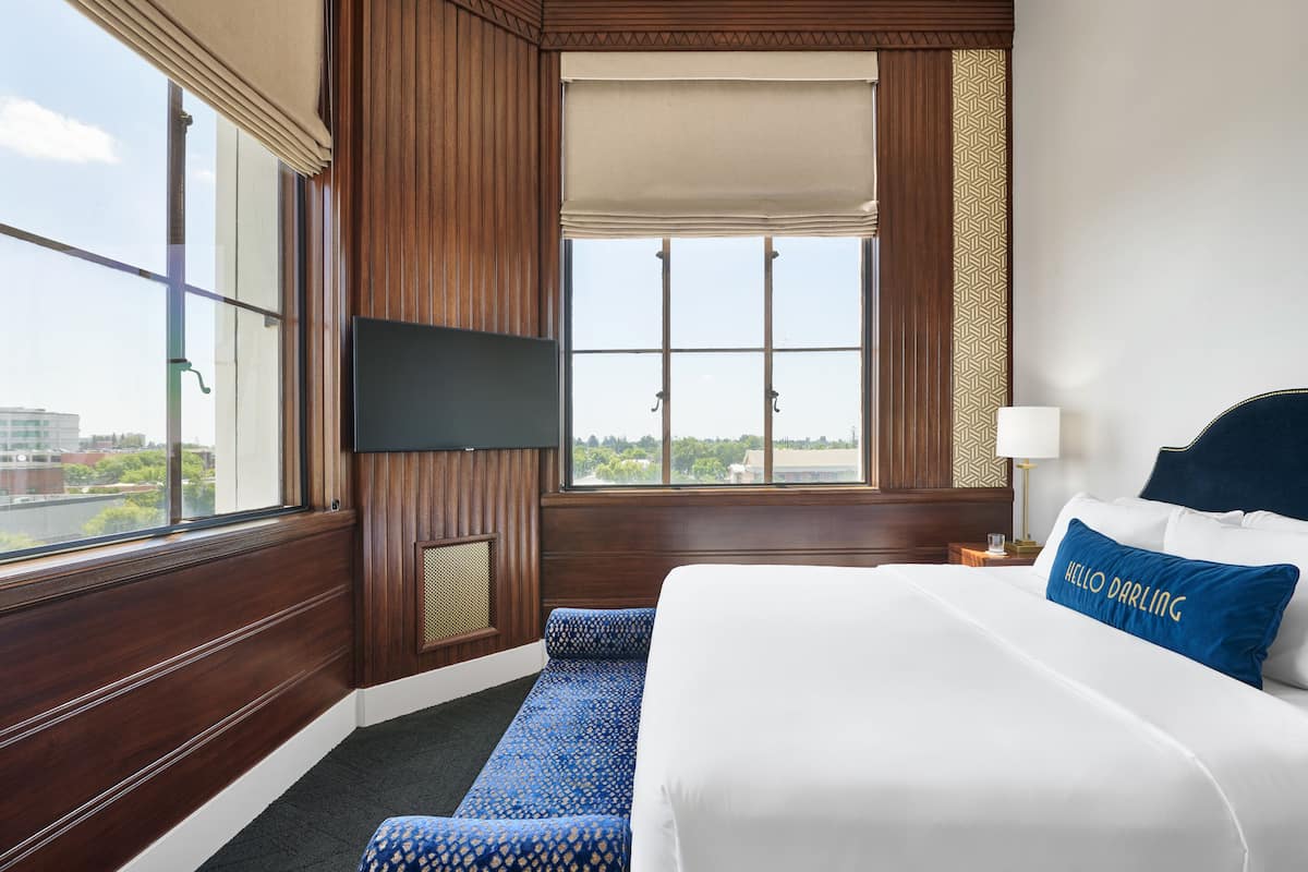 A hotel room with a large bed, a television mounted on the wall, and a window with a view of the city.