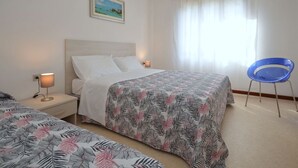 Ein Hotelzimmer mit Bett, Stuhl, Nachttisch, Lampe und einem Fenster mit durchsichtigen Vorhängen.