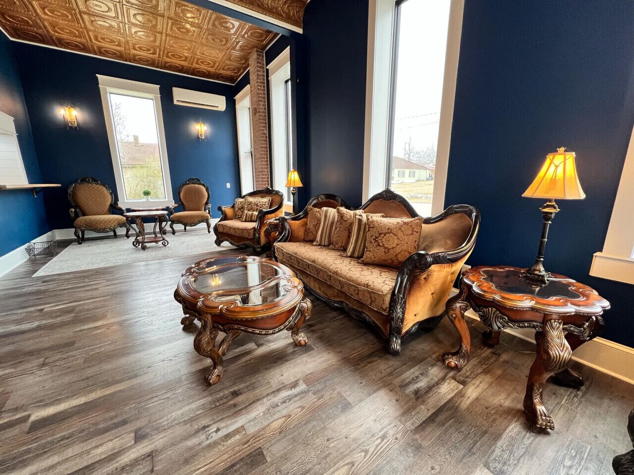 A room with a dark blue wall, a wooden floor, a sofa, two armchairs, a coffee table, and a lamp.