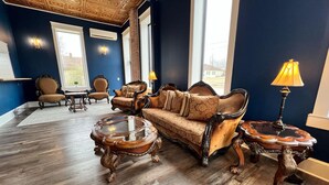 A room with a dark blue wall, a wooden floor, a sofa, two armchairs, a coffee table, and a lamp. - The Miser Lodge and/or Event Center (Cotter)