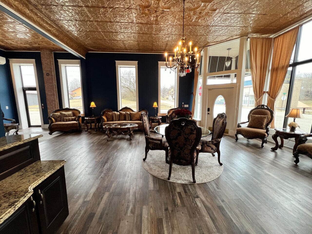 A spacious living room with dark wood flooring, a large chandelier, and multiple seating areas including sofas and armchairs.