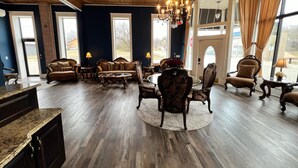 A spacious living room with dark wood flooring, a large chandelier, and multiple seating areas including sofas and armchairs. - The Miser Lodge and/or Event Center (Cotter)