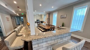 A modern kitchen with a granite countertop, a brick accent wall, and a dining area with a long bench and bar stools. - The Miser Lodge and/or Event Center (Cotter)