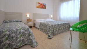 Hotellihuone, jossa on kaksi sänkyä, vihreä tuoli ja taulu seinällä.