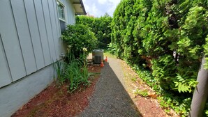 Um caminho de cascalho estreito leva a uma casa com um aparelho de ar condicionado e cones de trânsito laranja.