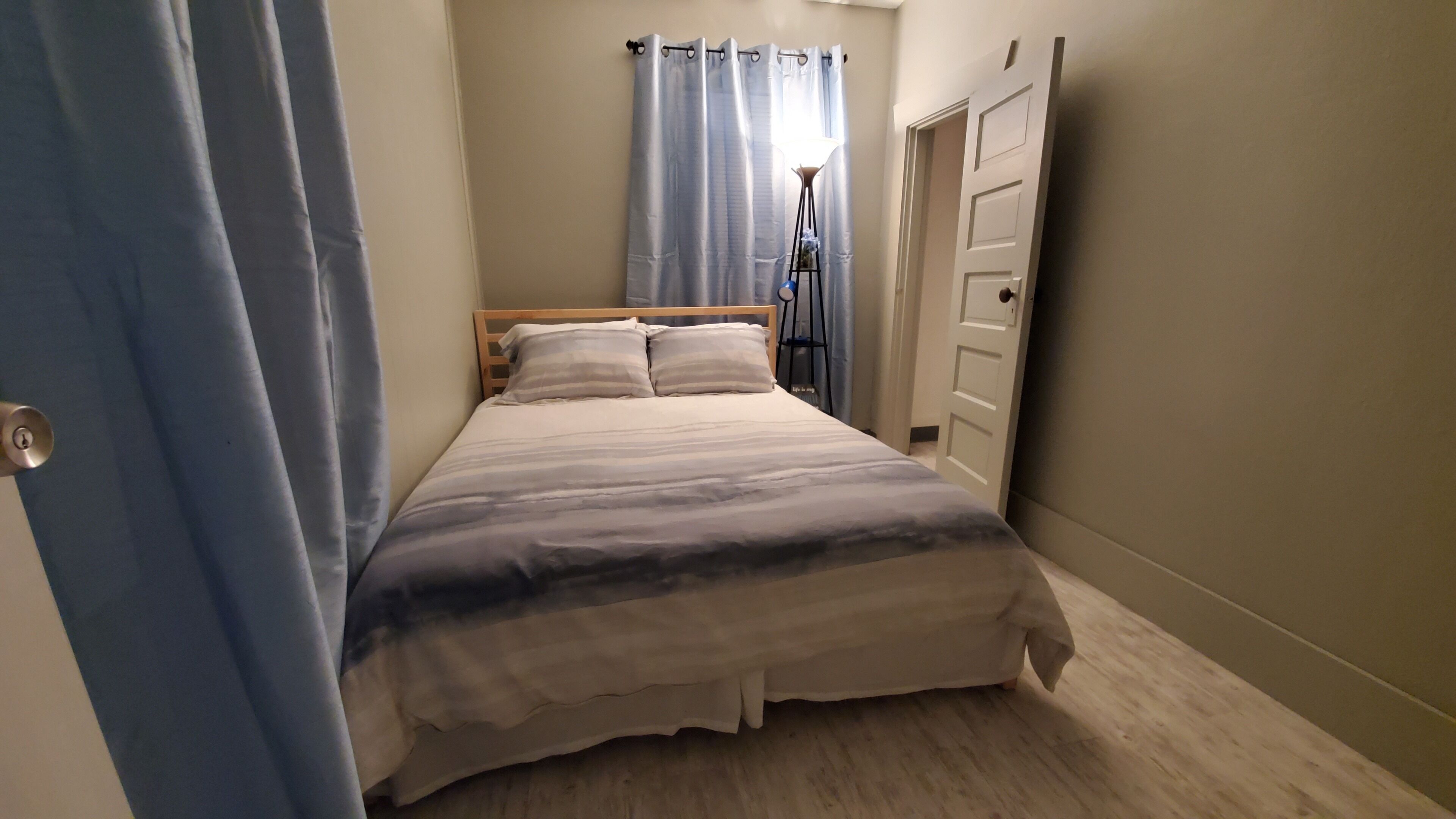 A bedroom with a bed, a door, and a window with curtains.