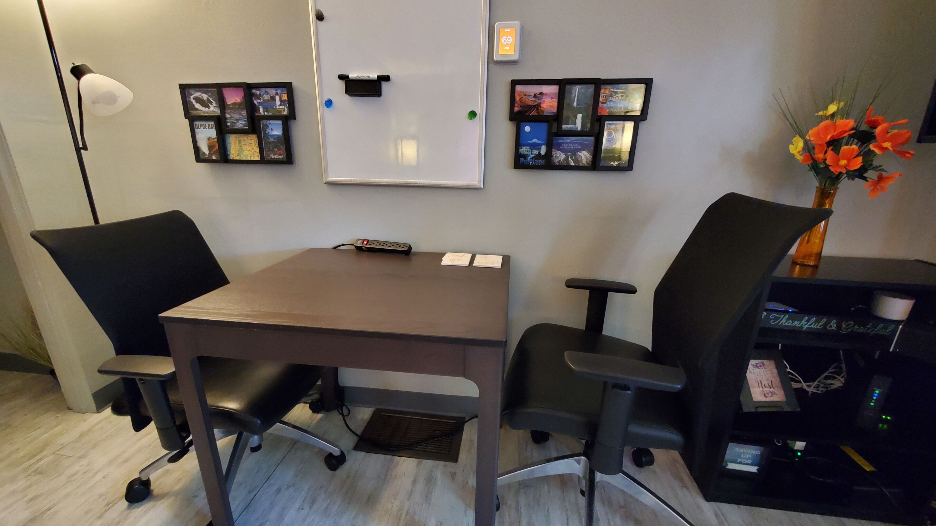 Een vergaderruimte met een tafel, twee stoelen, een whiteboard en een fotocollage aan de muur.