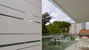A balcony with a glass railing, white chairs, and a table. - Lovely apartment for 5 people with pool, WIFI, A/C, TV, balcony and pets allowed (Lignano Sabbiadoro)