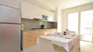 A modern kitchen with white cabinets, a granite countertop, and a dining area with a table set for two. - Lovely apartment for 5 people with pool, WIFI, A/C, TV, balcony and pets allowed (Lignano Sabbiadoro)