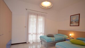 Ein Zimmer mit zwei Betten, einer Deckenleuchte, einem Gemälde und einer Tür.