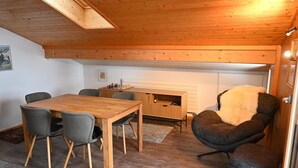A cozy room with a wooden ceiling, a dining table with chairs, a fireplace, and a comfortable armchair. - Beautiful apartment for 4 guests with TV, balcony and pets allowed (Lenk)