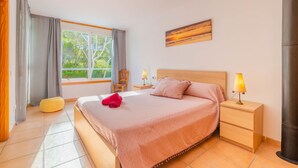 Una camera da letto con un letto, comodini, una lampada, una sedia, una finestra con tende e un quadro appeso al muro.