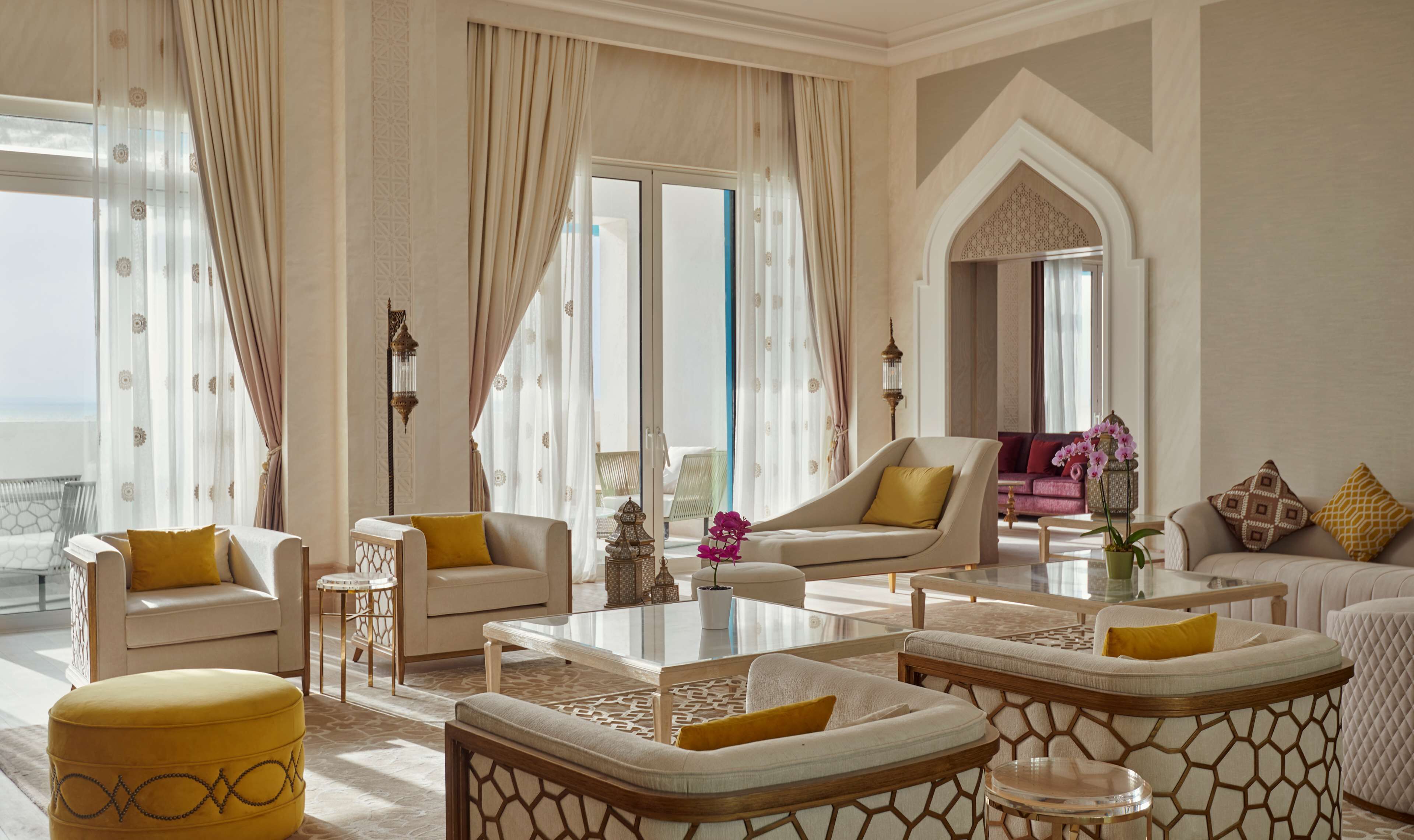 A spacious living room with a view of the sea, featuring a sofa, armchairs, a coffee table, and decorative elements like a lantern and potted plants.