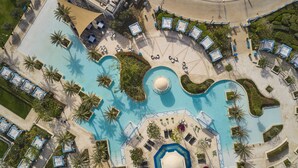 Vista aérea de un resort con varias piscinas, tumbonas y palmeras.