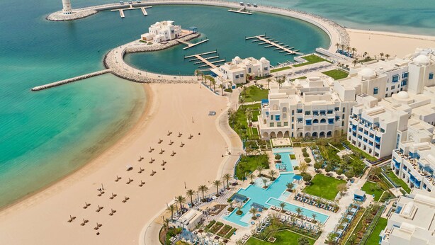 Vista aérea de un complejo turístico costero con playa, puerto deportivo y piscina.