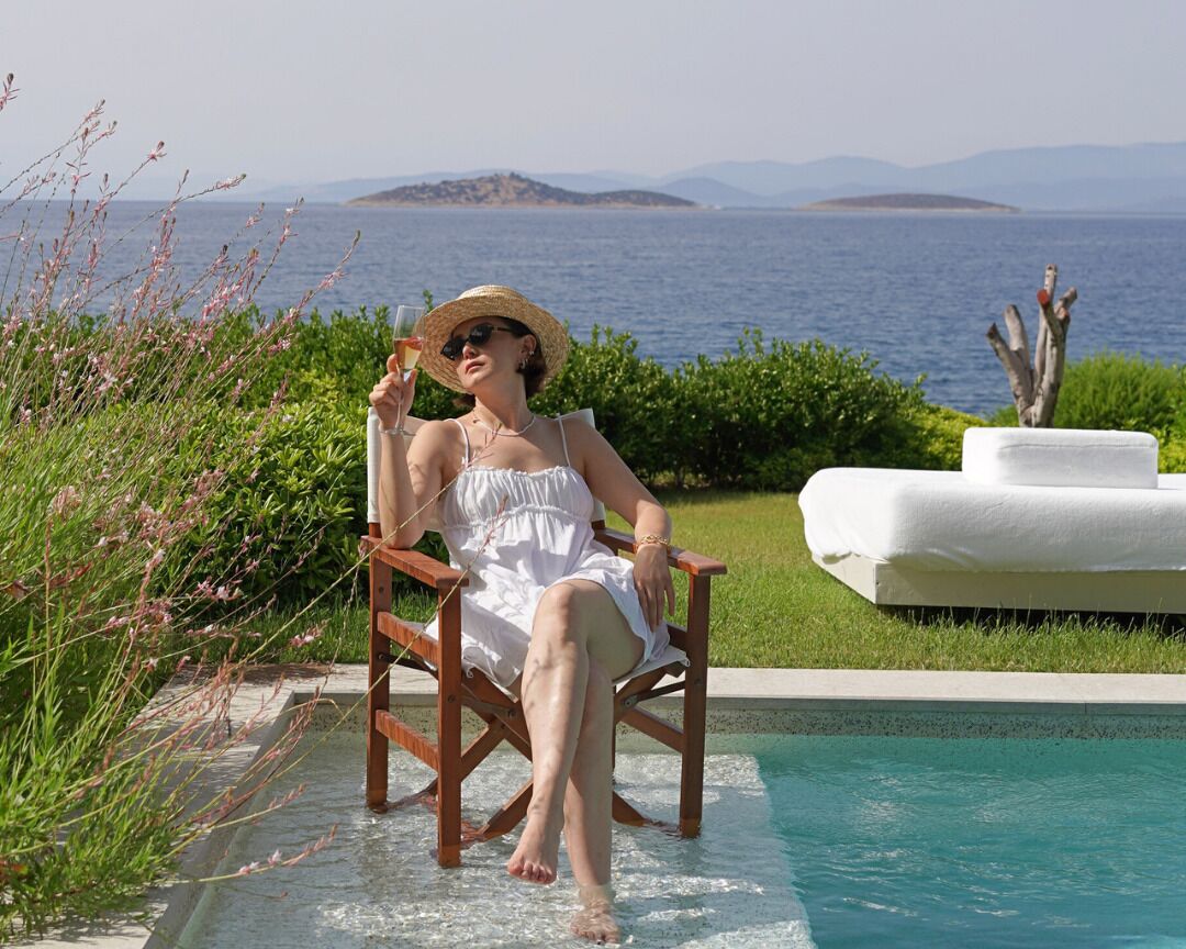 A person sitting by a pool with a view of the sea and mountains.