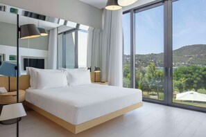Une chambre d’hôtel moderne dotée d’un grand lit, de tables de chevet, d’un bureau et offrant une vue sur un paysage verdoyant grâce à de grandes fenêtres.