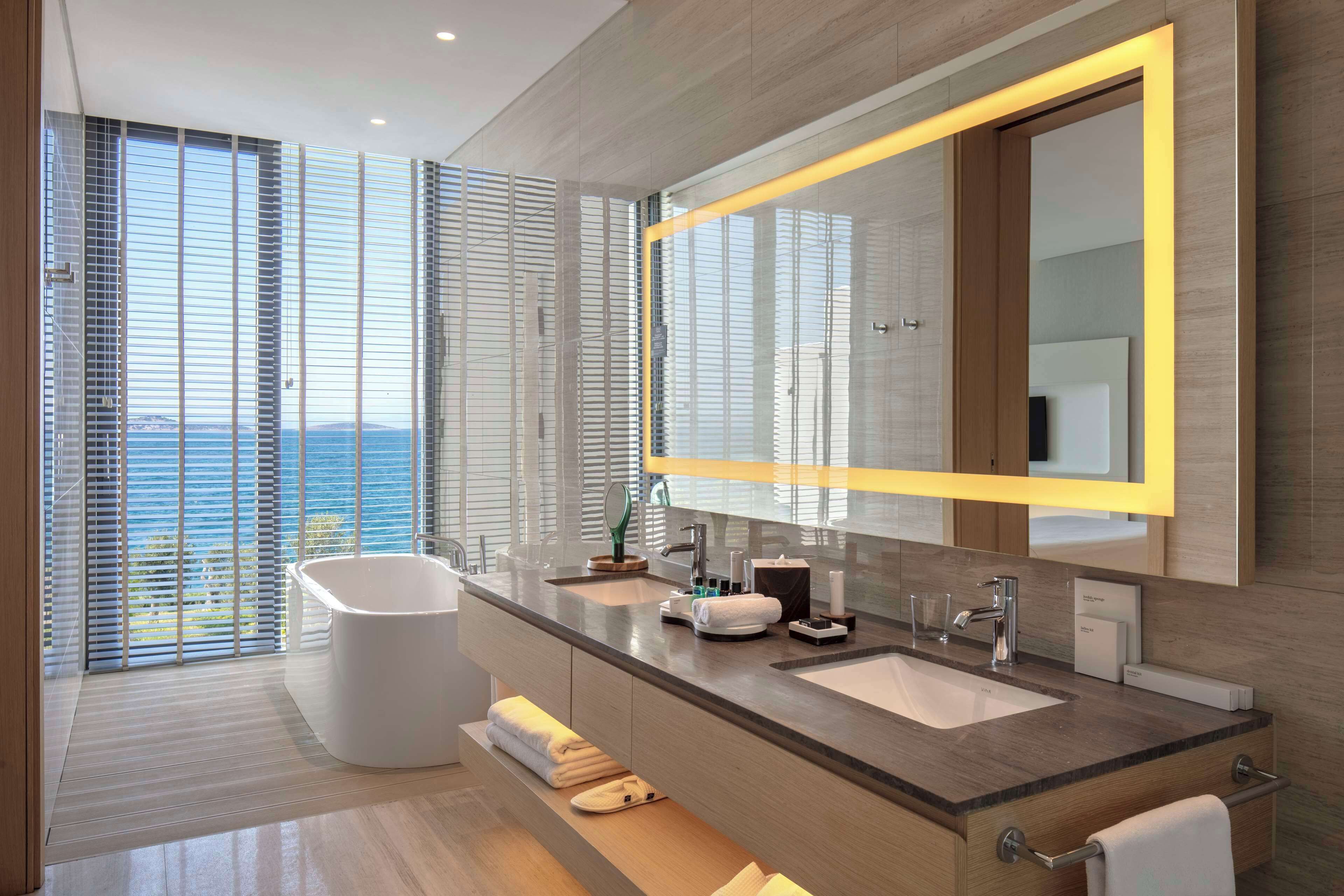 Un baño moderno con una bañera grande, lavamanos dobles y un espejo amplio con marco amarillo.