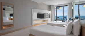 Een hotelkamer met een groot bed, een aan de muur bevestigde televisie, een balkon met uitzicht op zee en een grote spiegel.