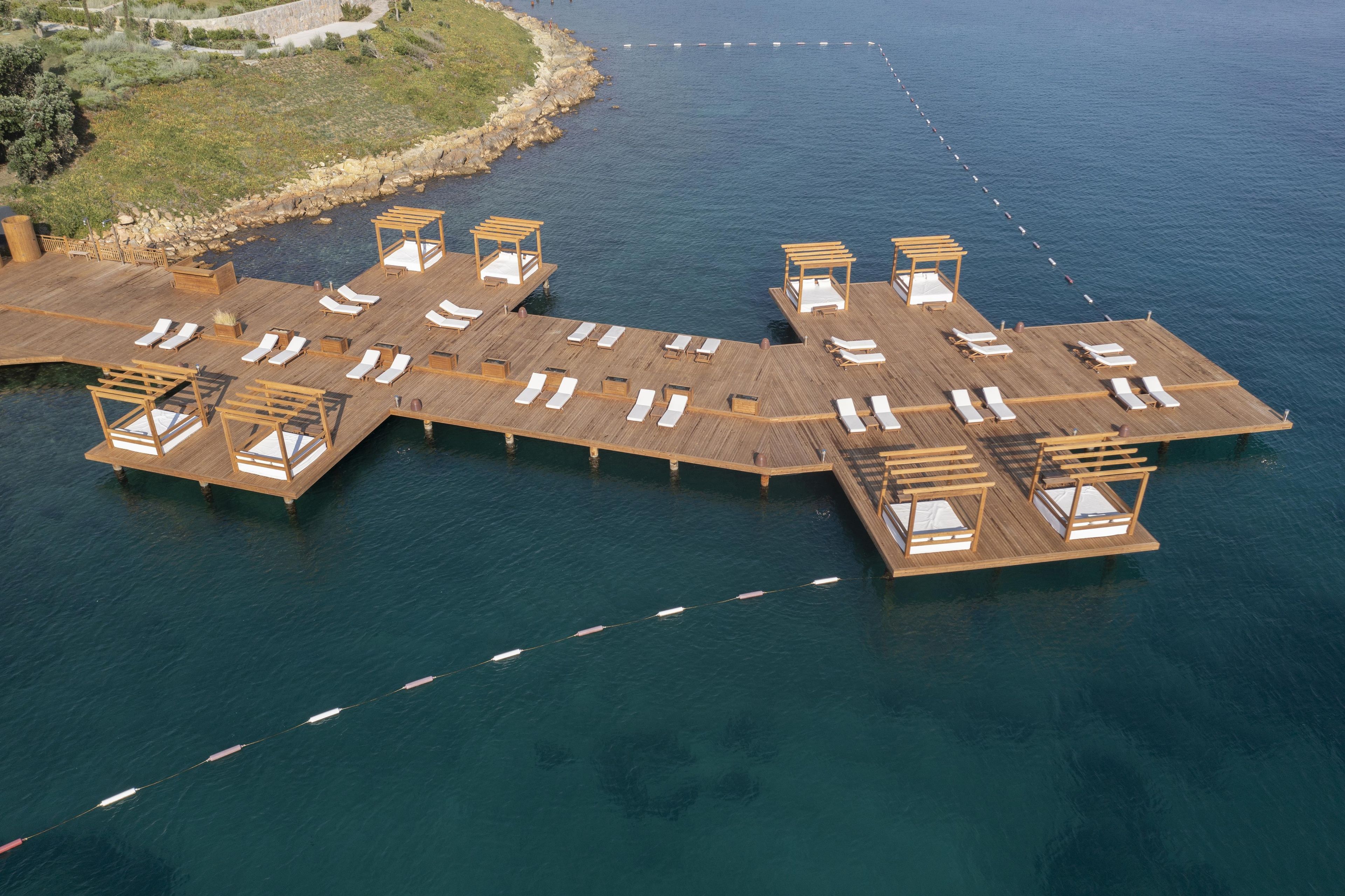 A wooden pier extending into a body of water with multiple sun loungers and wooden structures.
