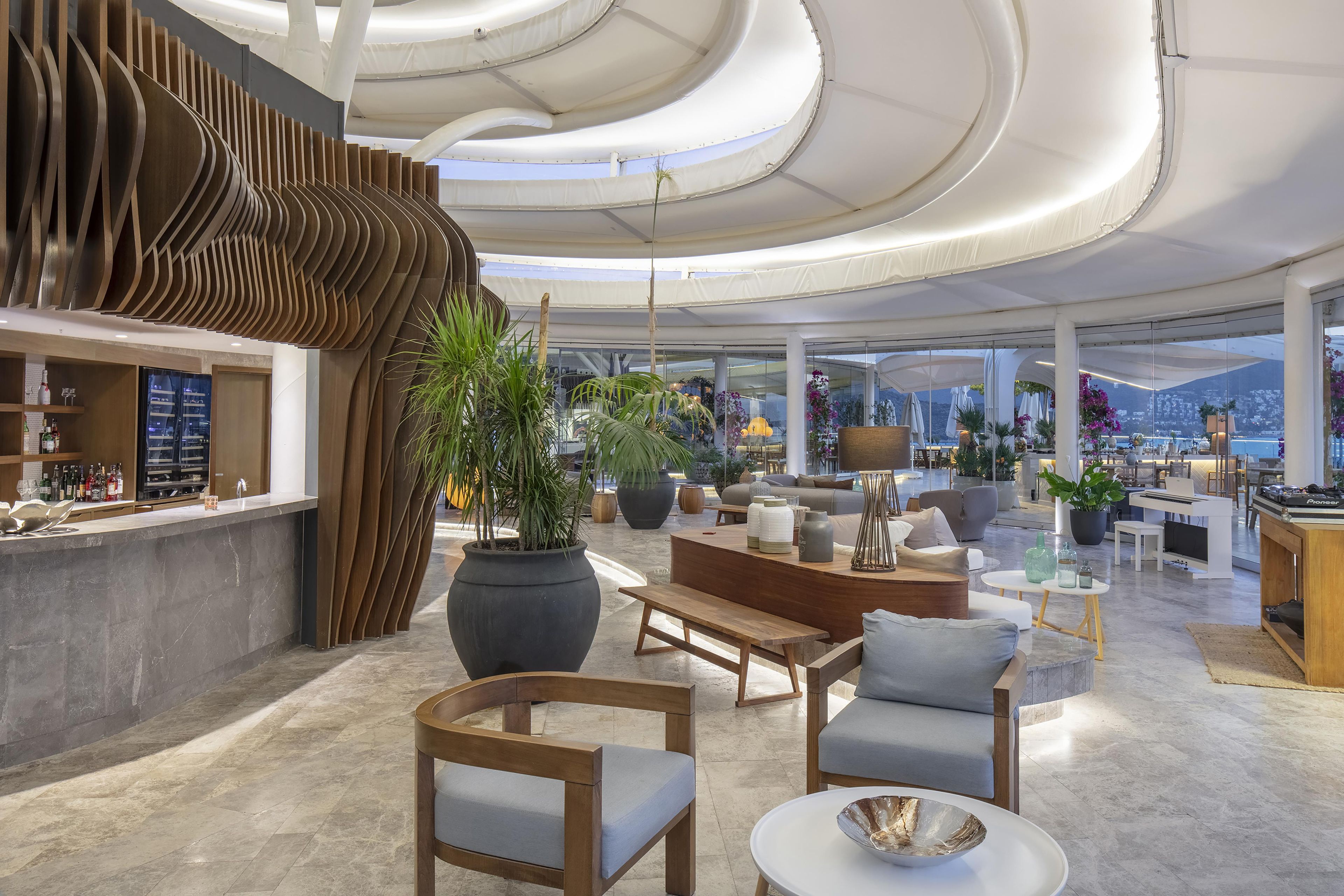 Amplia sala de estar con un diseño moderno, que incluye un bar, arreglos de asientos y grandes ventanales con vistas al exterior.