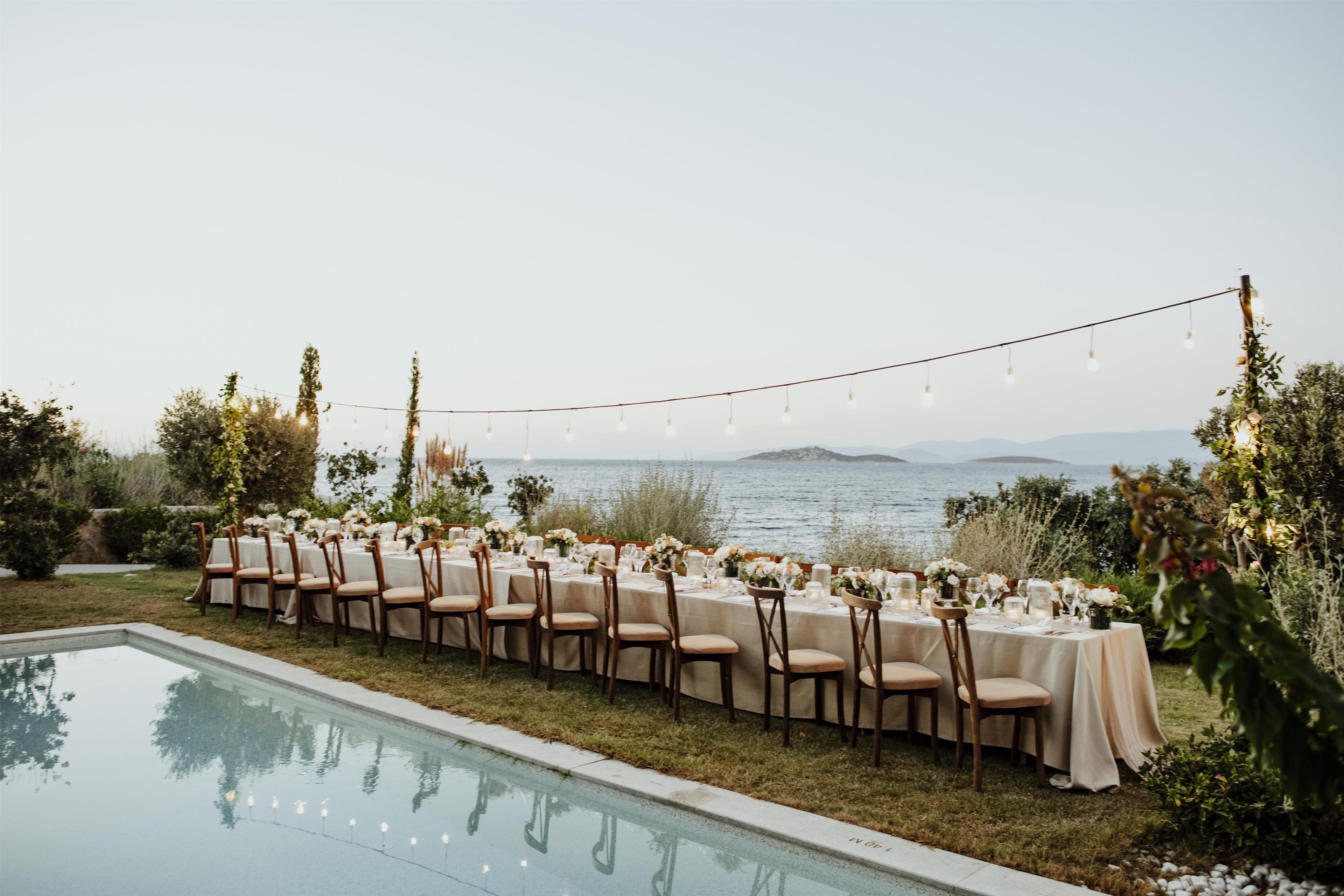 An outdoor dining setup by a pool with string lights overhead.
