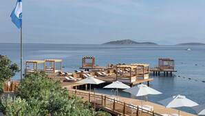 Un resort frente a la playa con mobiliario de madera en la terraza, sombrillas y una bandera.