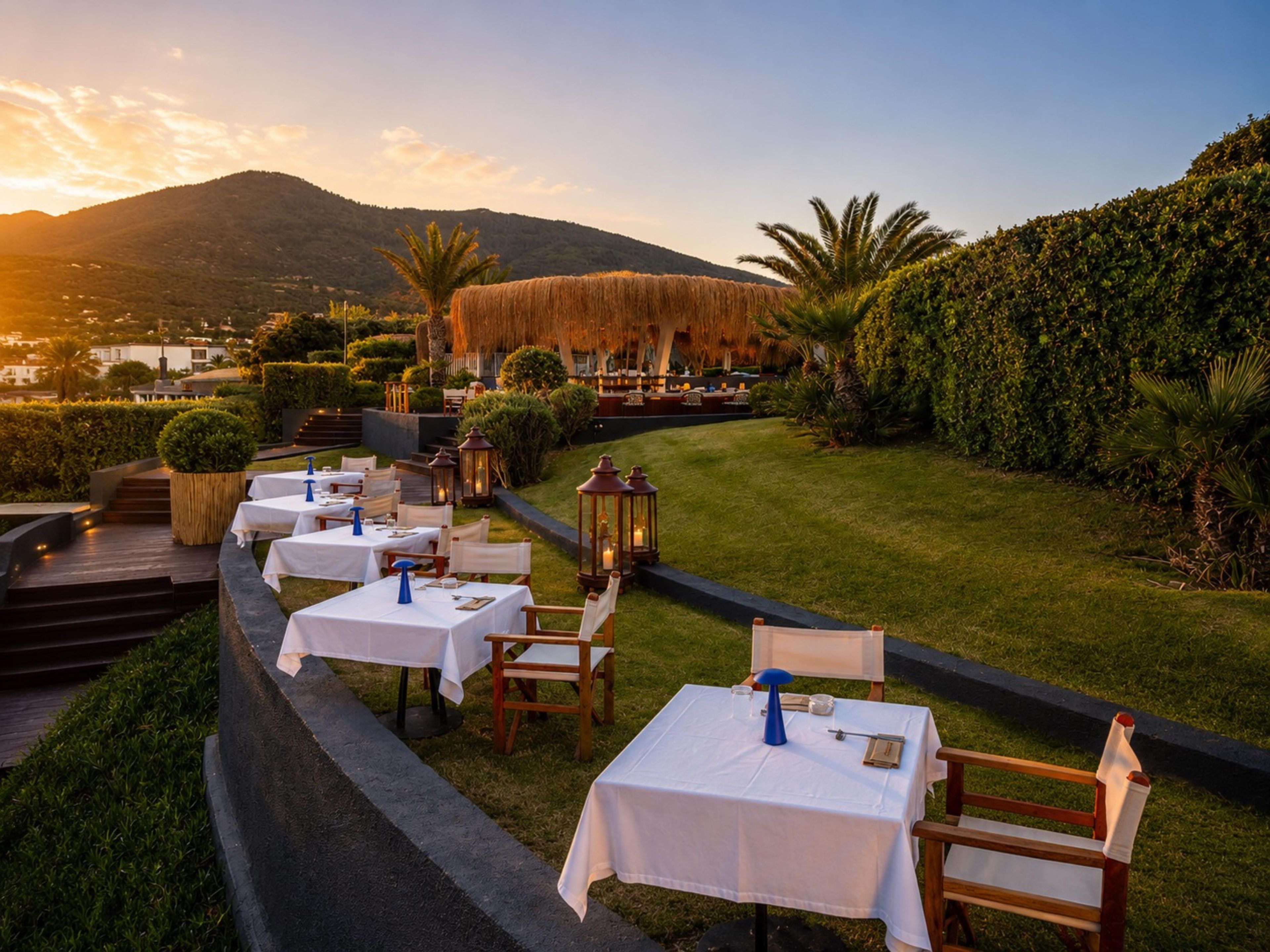 Un espacio de comedor al aire libre con mesas y sillas, rodeado de vegetación y un paisaje montañoso.
