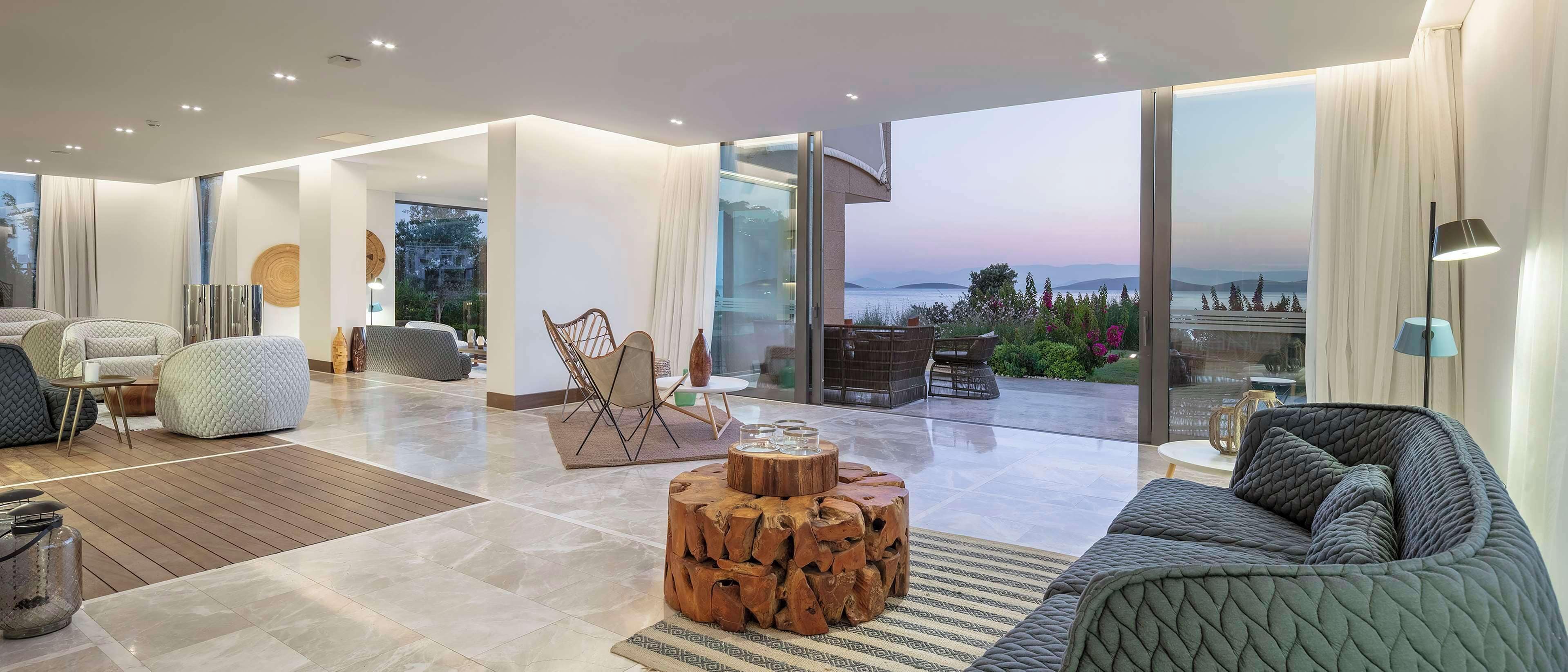 Un moderno salón con un gran ventanal que da a un balcón con vistas al mar.