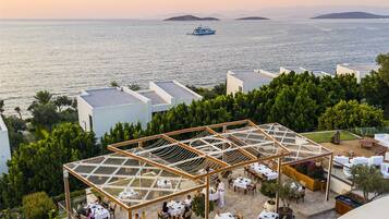 Un espacio al aire libre con mesas y sillas, rodeado de vegetación y vistas al mar.