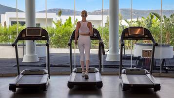 Un gimnasio con cintas de correr y una persona usándola.