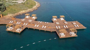 An aerial view of a wooden deck with multiple lounge areas over water, connected by walkways.