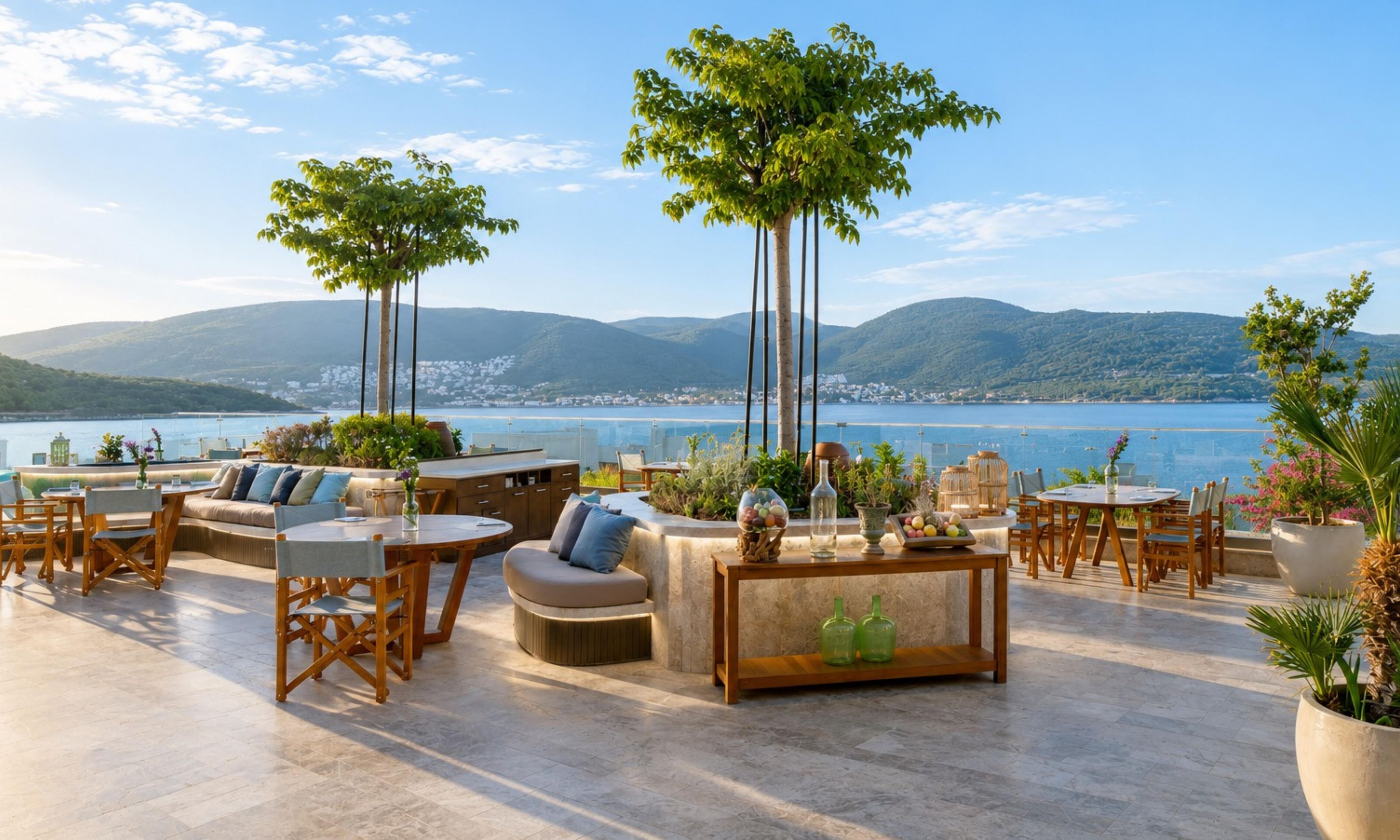 A terrace with outdoor seating, a view of the sea, and mountains in the background.