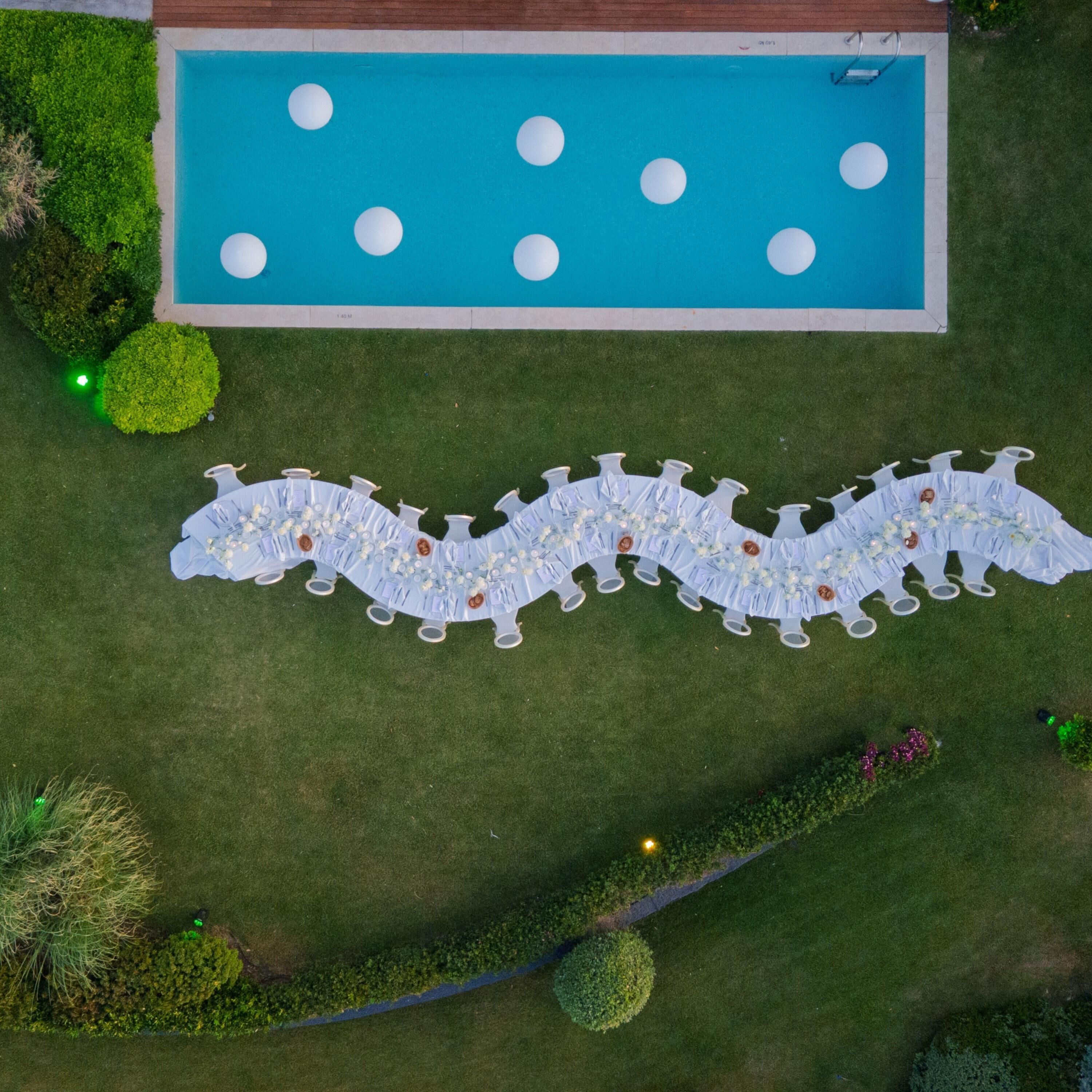 An aerial view of a swimming pool with a white deck, surrounded by well-maintained grass and small trees.