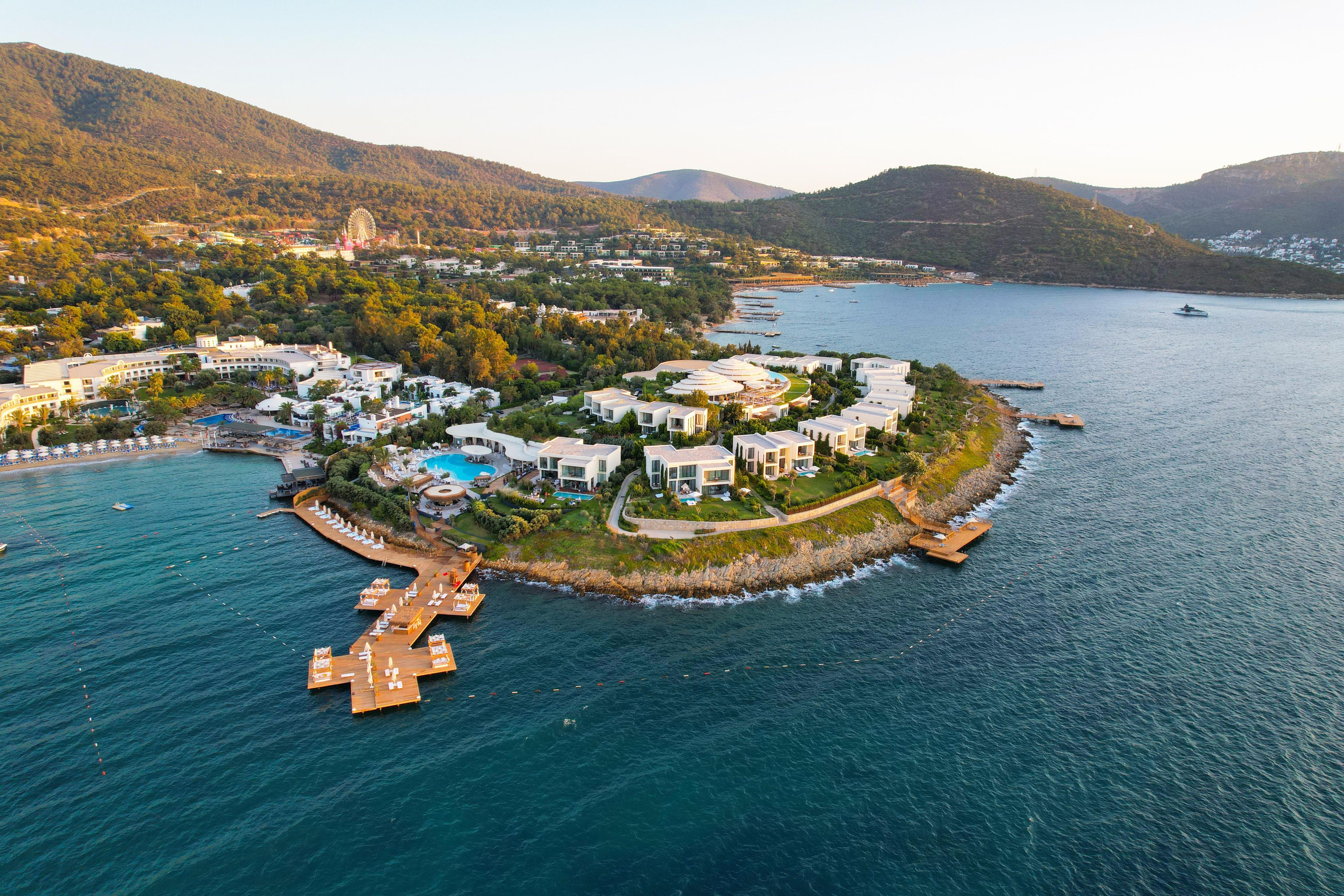 Vista aérea de un complejo turístico costero con villas, una piscina y un muelle.