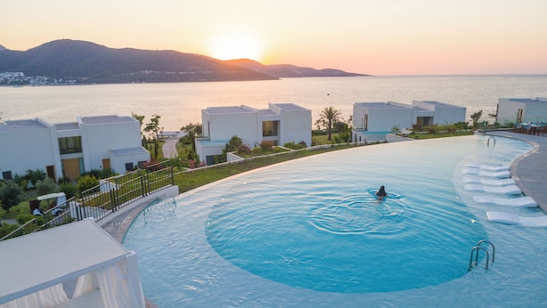 A resort pool with a view of the sea and mountains at sunset.