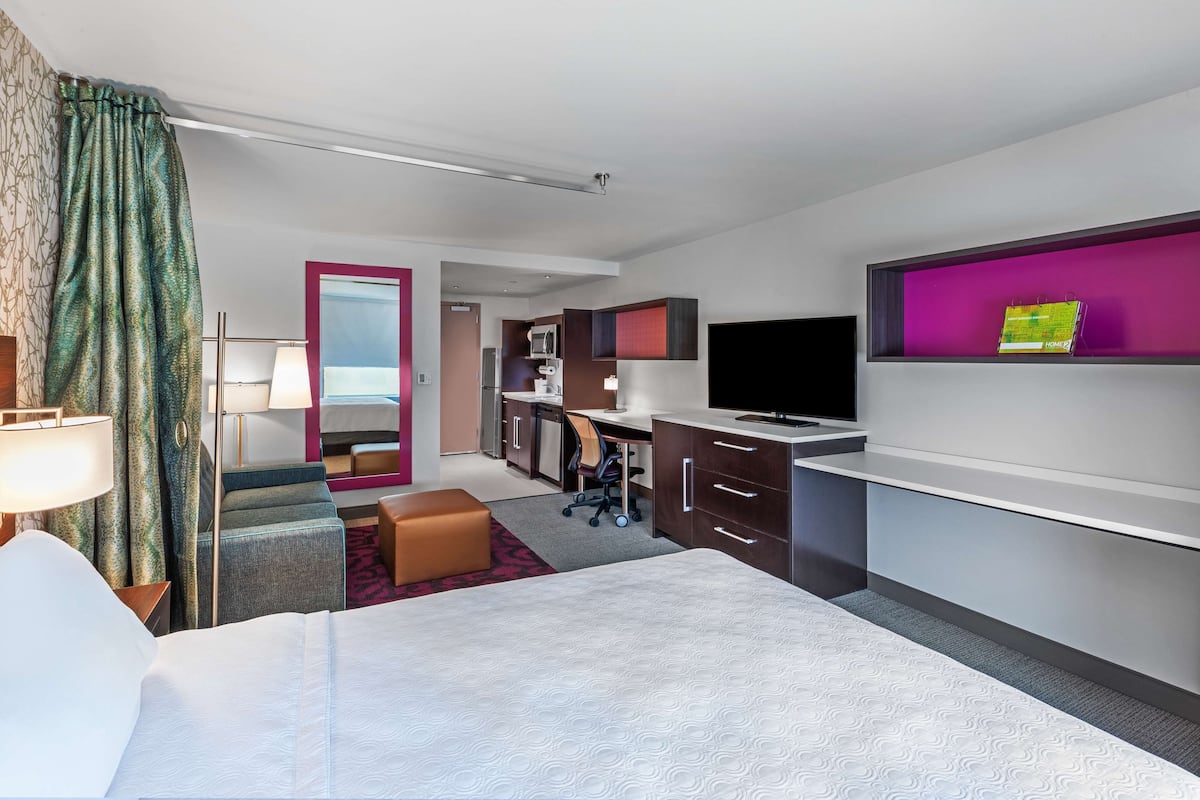 Une chambre d’hôtel équipée d’un lit, d’un bureau, d’une chaise, d’une télévision et d’une petite kitchenette.
