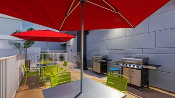 Un patio al aire libre con una parrilla, sillas verdes y una sombrilla roja.