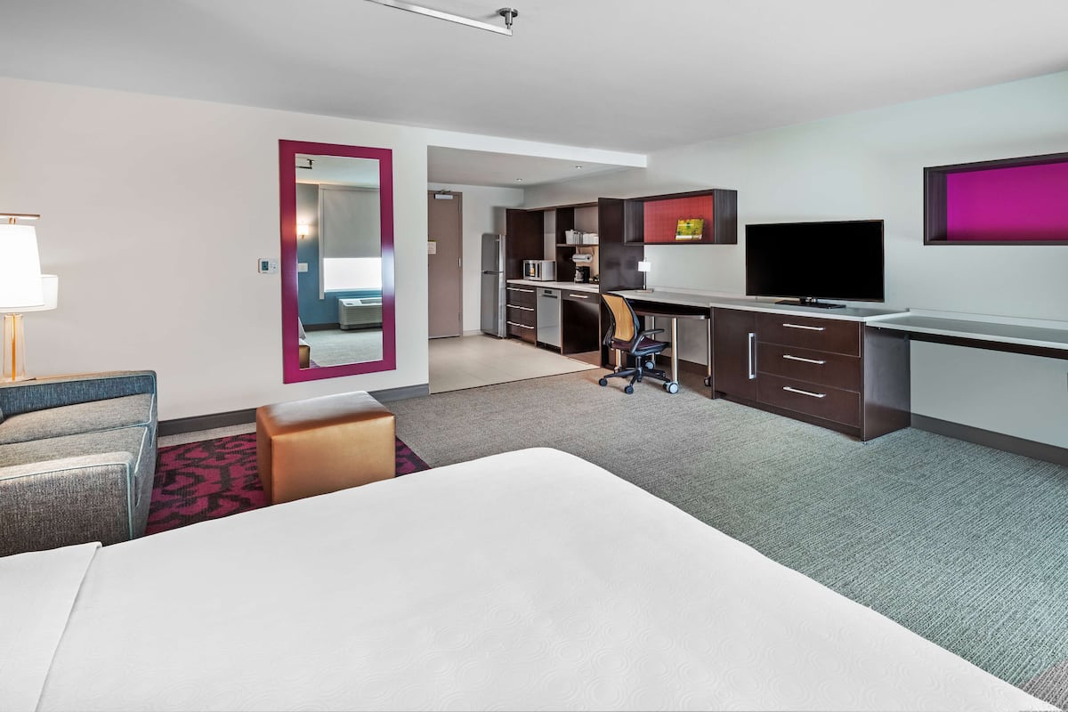 Une chambre d’hôtel équipée d’un lit, d’un bureau, d’une chaise, d’une télévision, d’un miroir et d’une kitchenette.