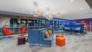 A modern lounge area with seating arrangements, including a blue sofa and red chairs, and a large window offering a view of the outside. - Tru by Hilton Laredo Airport (Laredo)