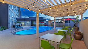 An outdoor pool area with a covered seating area, poolside tables, and chairs. - Tru by Hilton Laredo Airport (Laredo)