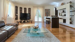 Un salon spacieux avec un canapé en cuir, une table basse en verre, un téléviseur et un coin repas doté d’un bar.