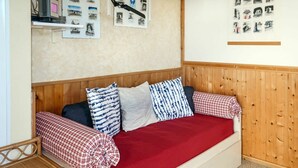 Ein gemütliches Zimmer mit einem Holzkopfteil, einem roten Sofa mit gemusterten Kissen und einem kleinen Holztischchen mit Büchern.